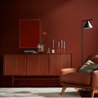 Modern living room with a wooden sideboard, brown armchair, and decorative items against a red wall.